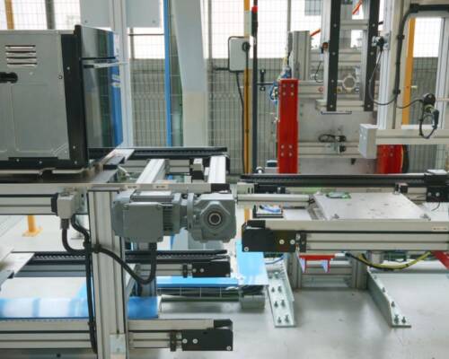 Pallet change station that transfers the product from the assembly pallet to the electrical-test pallet, with automated pallet return, inside the Movin-built home appliance assembly line